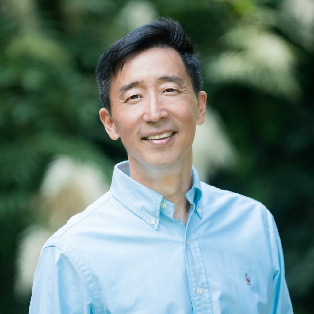 Photo of Ken Shigamatsu, a Japanese man, wearing a light blue shirt, smiling.