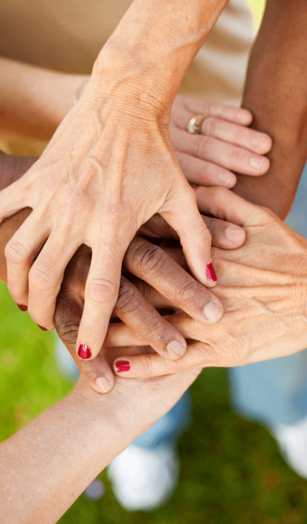 Photo shows multiple hands all clasped together.